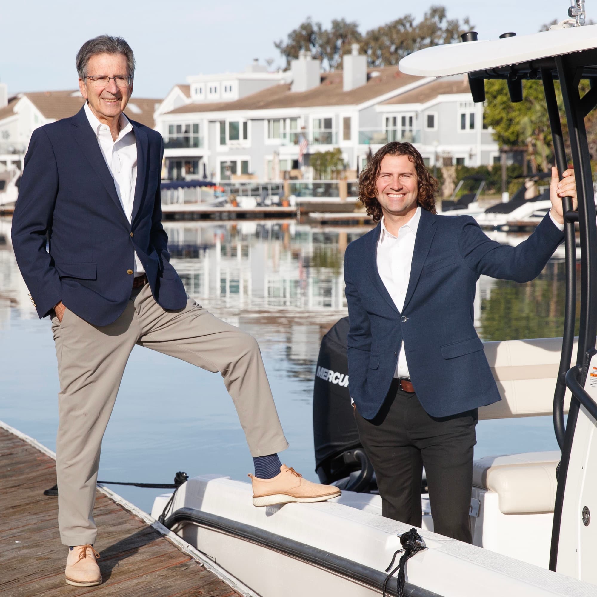Craig and Justin Ratowsky on a Huntington Harbour dock with waterfront homes and boats behind them, Ratowsky Group at Compass luxury waterfront specialists.