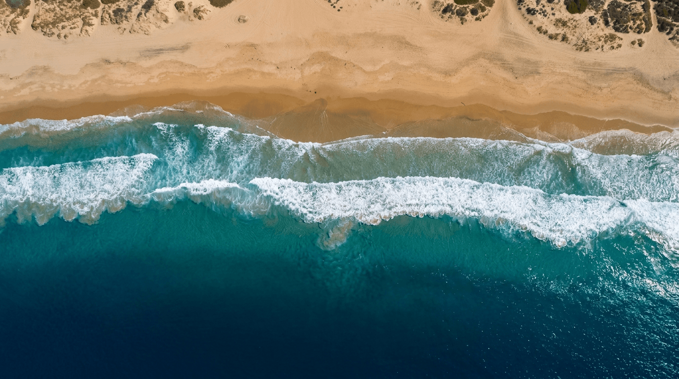 Top-down aerial view of turquoise Pacific surf meeting a wide Southern California beach.