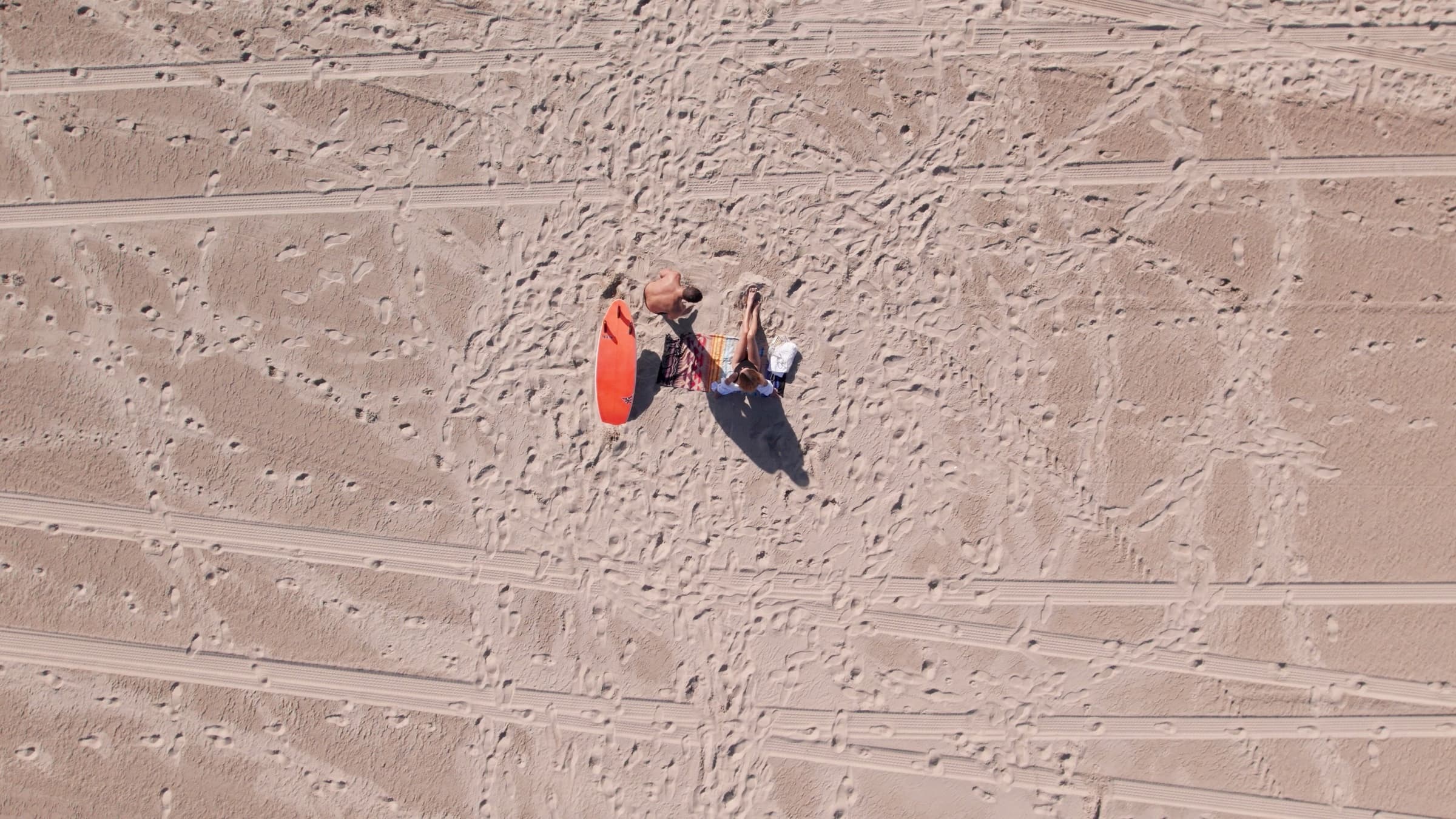 Overhead view of sunlit sand and the foam edge where the Pacific meets the Huntington Beach shore.