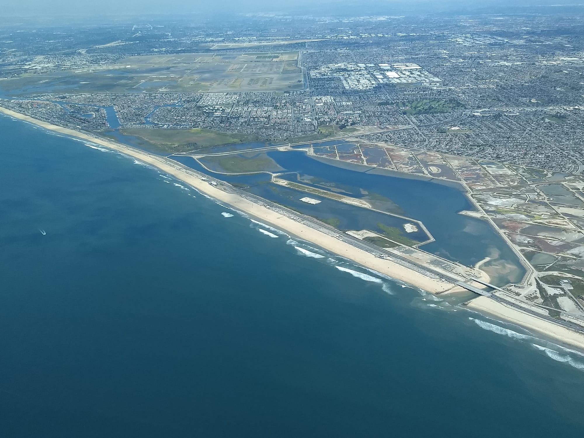 Aerial looking north over the Bolsa Chica Ecological Reserve wetlands, beach and coastline, with neighborhoods inland.