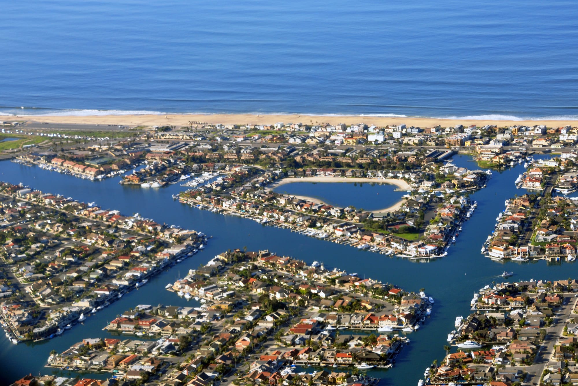 Aerial of Huntington Harbour islands, waterfront homes and boat docks, with Sunset Beach and the ocean beyond.