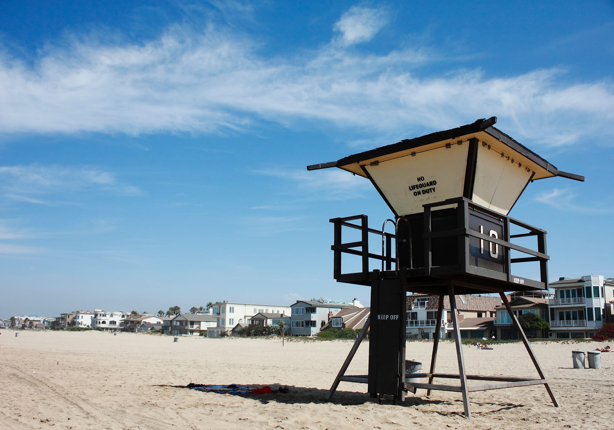 Lifeguard tower 10 on the sand at Sunset Beach, with beachfront homes behind it under a blue sky.