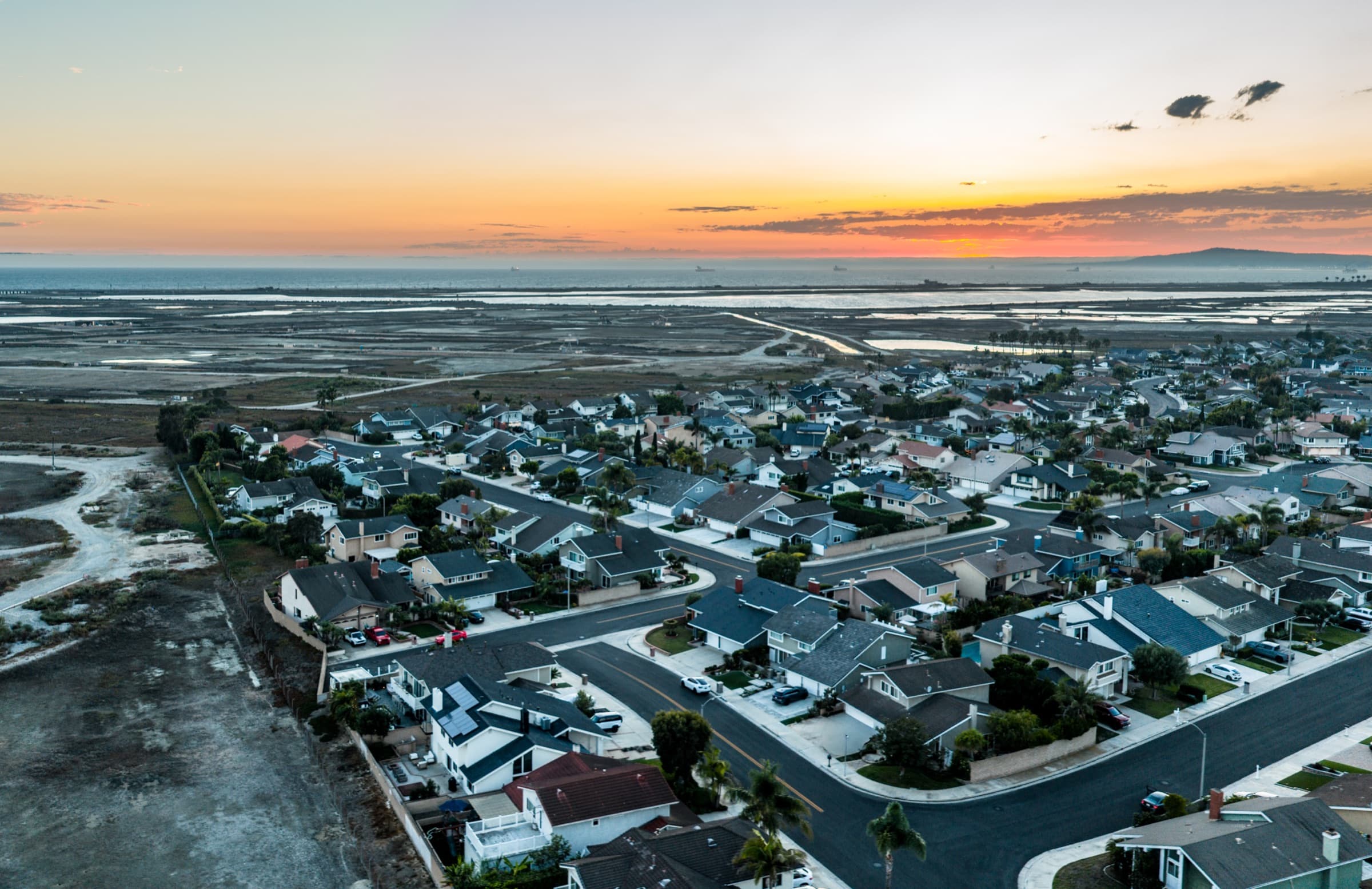 Sunset aerial over The Landing tract in northwest Huntington Beach, homes beside the Bolsa Chica wetlands with the Pacific beyond.