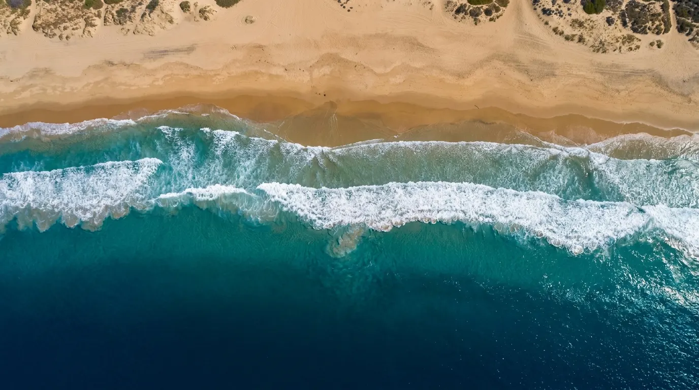Top-down aerial view of turquoise Pacific surf meeting a wide Southern California beach.