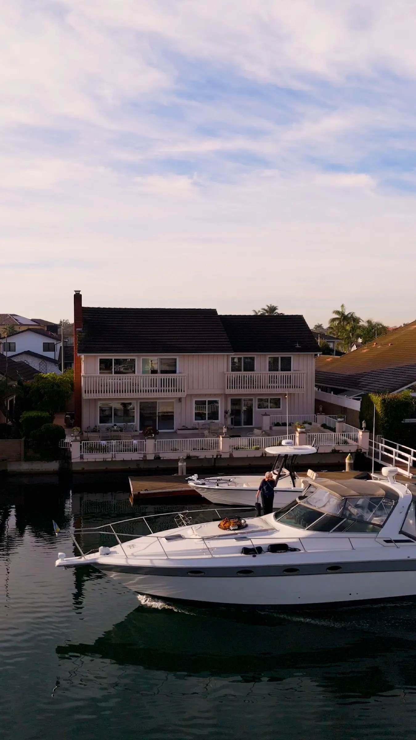 Golden-hour view of a yacht moving through Huntington Harbour past waterfront homes and private docks.